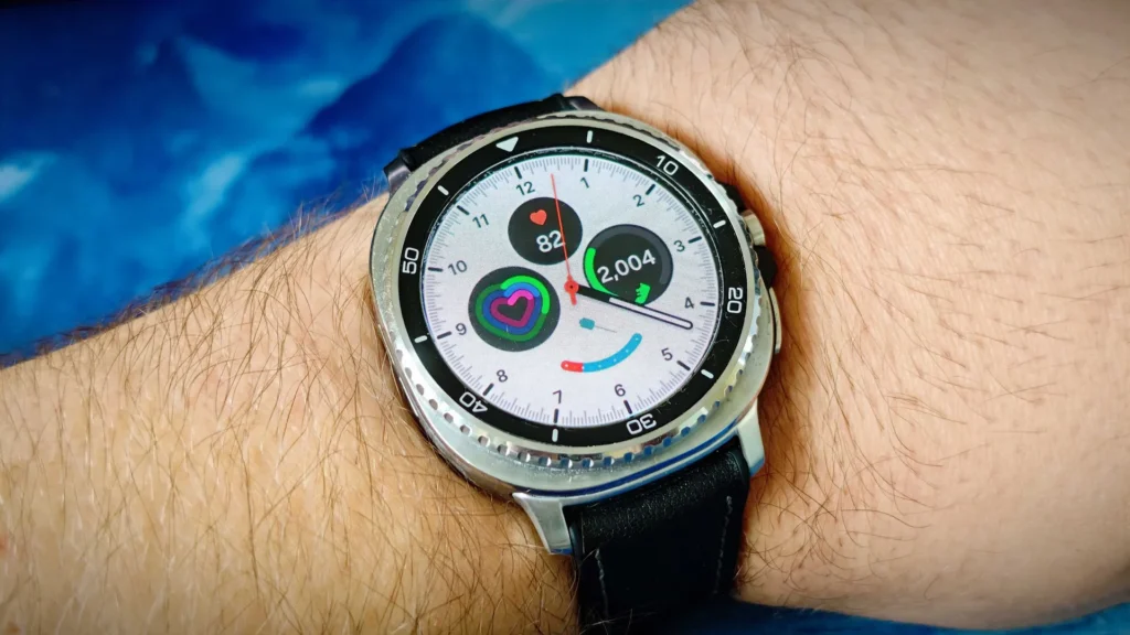 Samsung Galaxy Watch8 Classic smartwatch showing a circular silver rotating bezel and leather-feel hybrid band, displaying a bright analog-style watch face.
